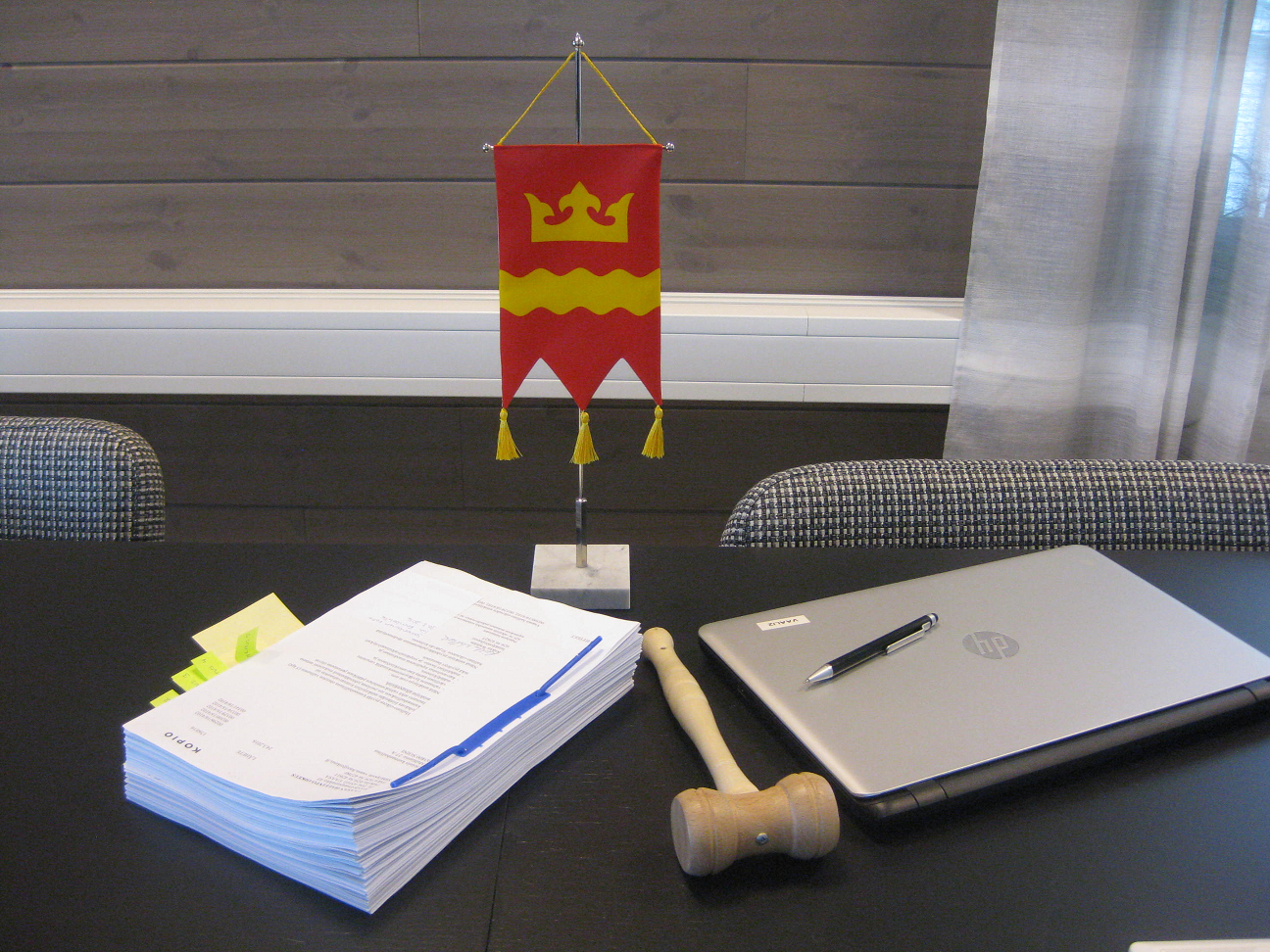 Kuva: Kuvassa on Soinin kunnan viiri, puheenjohtajan nuija, esityslista ja tietokone valtuustosalin pöydällä